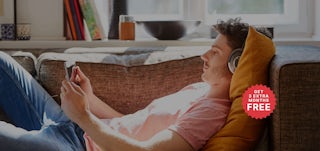 Man on couch with device and headphones. Kodi hero super desktop with 12+3 badge.